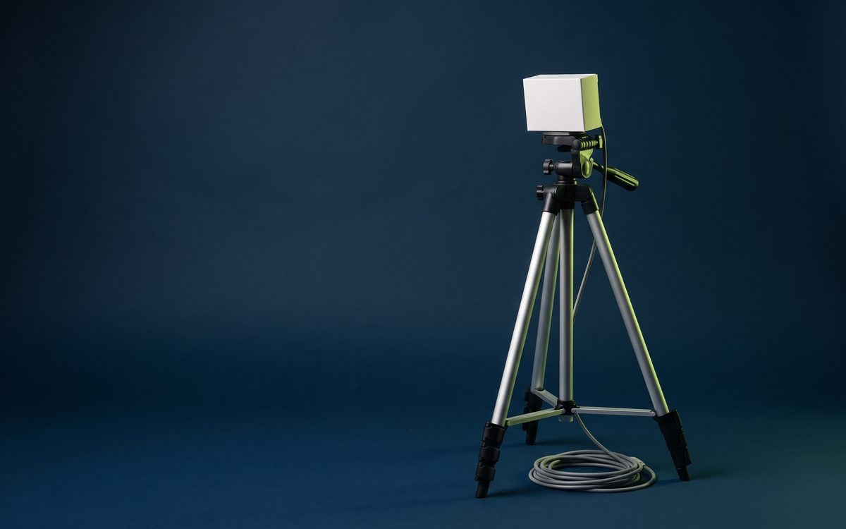 Illustration: a lightweight tripod carrying a small plain white box, its cable coiled at the feet, on a navy backdrop.