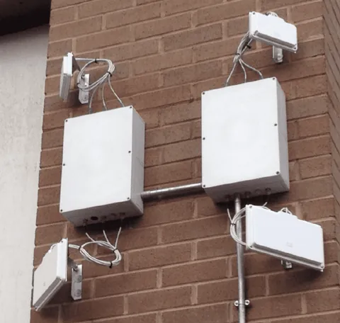 Two white DW WiFi enclosures on a brick wall, with patch antennas on brackets and conduit between them.